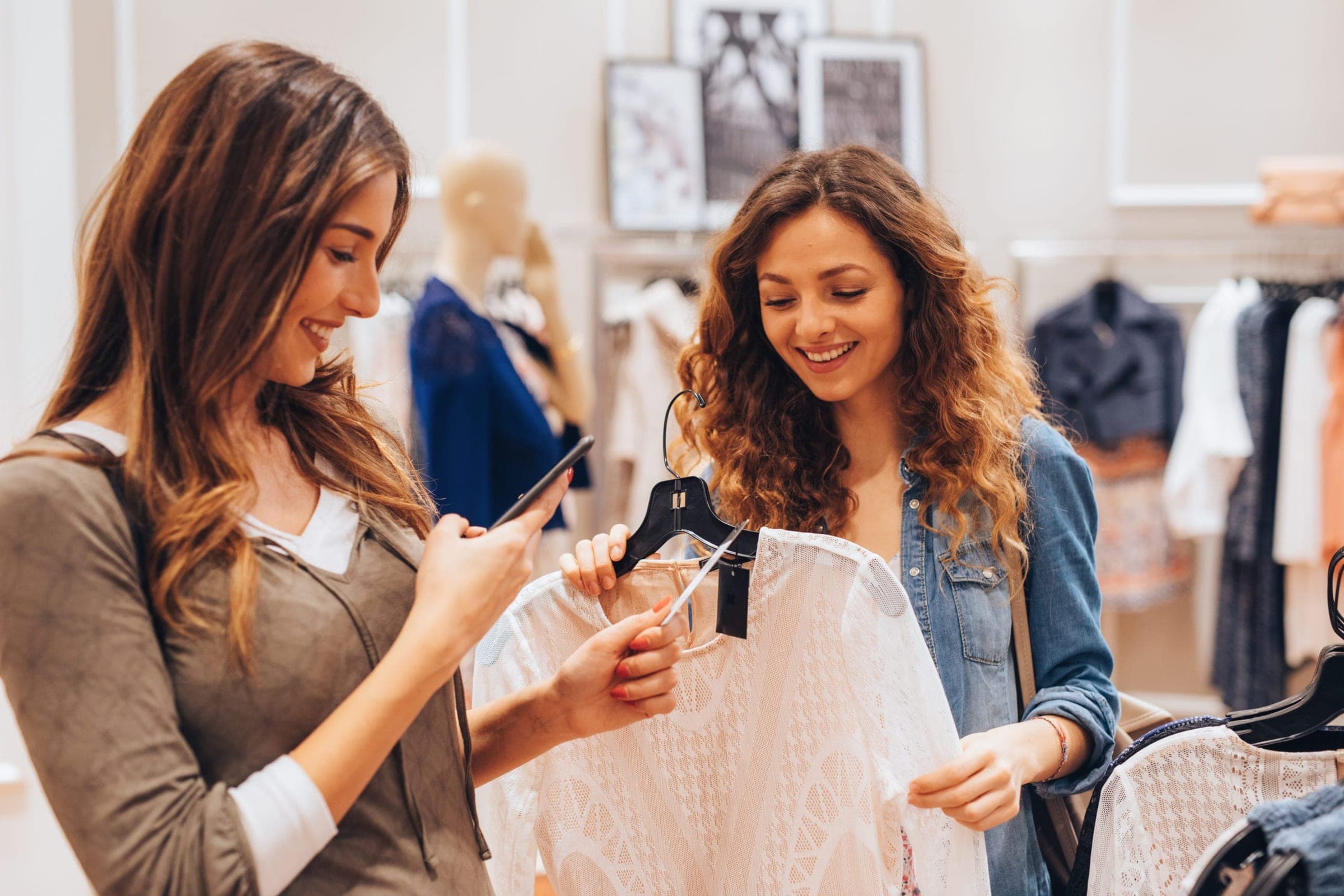 Woman taking a picture of the price tag of a dress while shopping with her friend.