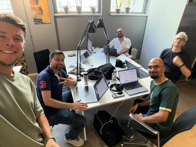 Five colleagues working on laptops around a shared desk in the office